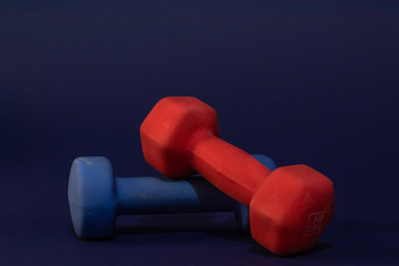 dark view of two Hand weights, red and blue, each of Five pounds, close-up on dark blue background