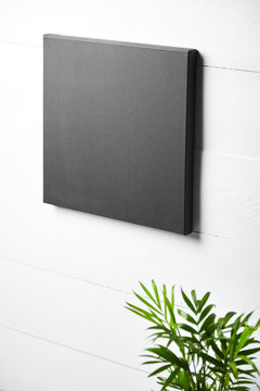 A black cotton canvas and green plant on white wooden background. Stretched clean canvas hanging on wall. Mock up, side view