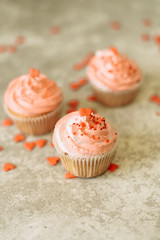 Pink cupcakes on a gray background for Valentine's day. Gift sweets with cream and sprinkle with hearts