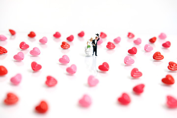 Miniature / toys photography for valentines day - bride and groom with heart shape and love word beads on shiny white background