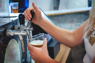 Bartender girl standing, pours beer into a large cup