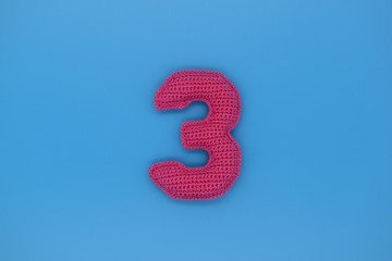 Number 3 is knitted from yarn on a blue background.