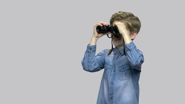 Happy excited boy looking through binoculars. Surprised little explorer using binoculars against gray background. Kid exploration concept.