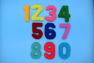 1, 2, 3, 4, 5, 6, 7, 8, 9, 0. Multicolored numbers on a blue background are knitted from yarn.
