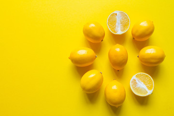 Top view whole and sliced ripe lemons laid out in the shape of a dial on a yellow surface, concept of health and vitamins