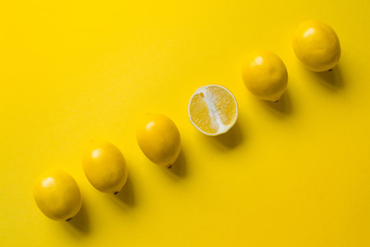 Top view whole and sliced ripe lemon slaid out in a row on a yellow surface, concept of health and vitamins