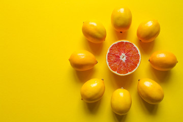 Top view whole and sliced ripe lemons and grapefruit laid out in the shape of a dial on a yellow surface, concept of health and vitamins