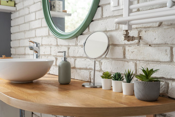 Bathroom in modern style with wooden counter, ceramic wash basin, round mirror, brick wall and succulents. Scandinavian design and minimalism in apartment.