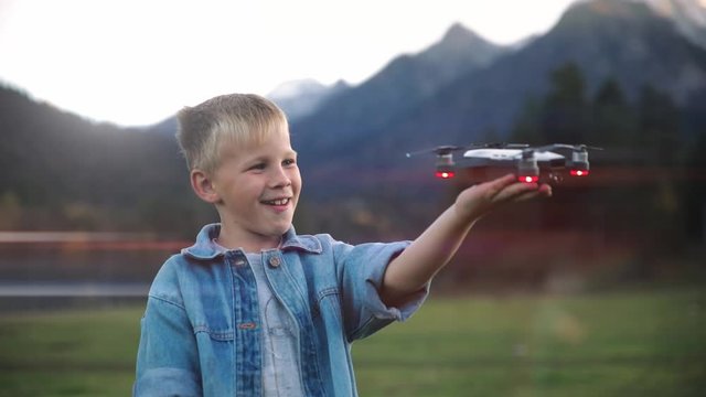 Slow motion a happy boy very happy and smiling gift the background of a bright sky and mountains holds a white quadro copter drone plane in his hand and start him playing . lifestyle. Lens flare