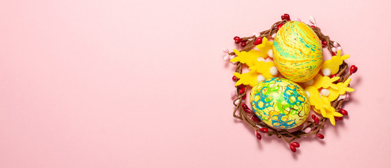 Banner of Easter eggs, yellow rabbits inside a woven wreath on pink background at the right side with copy space. Fat lay top view. Easter concept.
