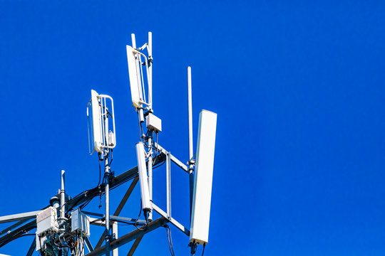 A close up and detailed view of electronic communication equipment atop a cell site tower, multiple white antenna and RRH, Remote Radio Head, with copy space