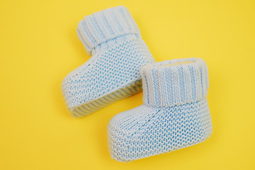 Small cute knitted booties for newborn baby. Baby shoes on yellow background. 