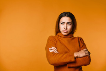 View of thoughtful young caucasian girl dressed in pullover  of ocher colour  on the orange...