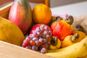 fruits in wooden basket: cashew, orange, grape, banana, mango and papaya