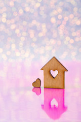 Obraz na płótnie Canvas Wooden icon of house with hole in form of heart on glitter shiny light and pink background with bokeh lights.