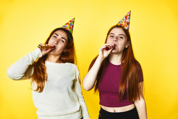 Two young girls wearing birthday hats stand on the yellow banner background
