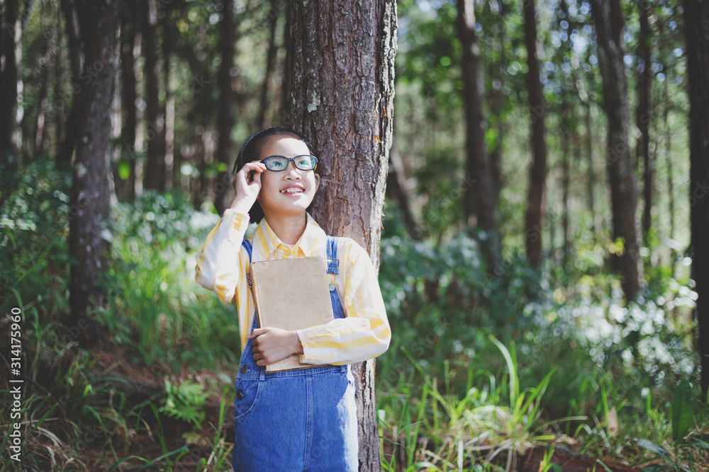 Wall mural cute child girl with glasses dreaming in summer with holding book