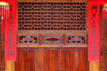 The old traditional style wood carving door with Spring festival couplets during Chinese new year.The text on scrolls  means Hundreds of flowers in bloom in springtime and Good luck will come to home