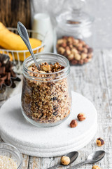 Chocolate banana granola with nuts in a glass jar on a light background