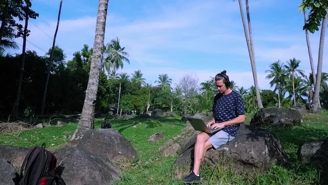 A man is sitting on the stone while working as a freelancer. He is doing his work in the mountain.