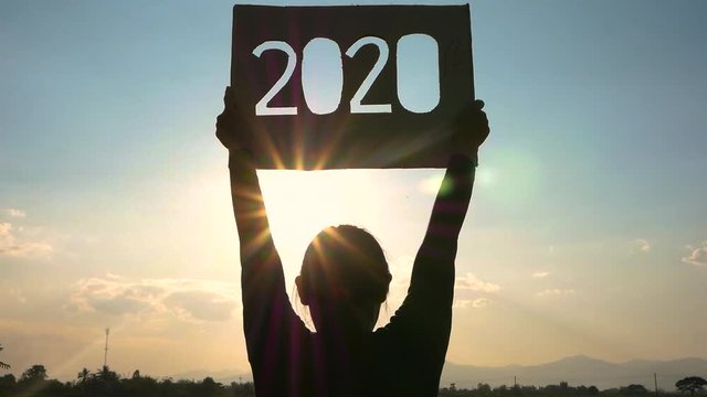 Silhouette of woman holding recycle cardboard with 2020 text over sunset sky background and the sunshining through the text. Concepts of New Year and celebration.