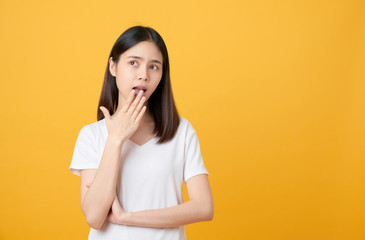 Doubt Asian woman hands covering mouth on yellow background.