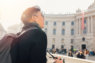 Young Asian man tourist taking photos with camera in hands near Hofburg palace in Vienna, Austria,...