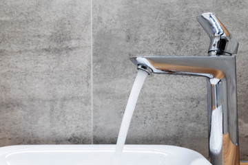 faucet with running water in bathroom with tile wall