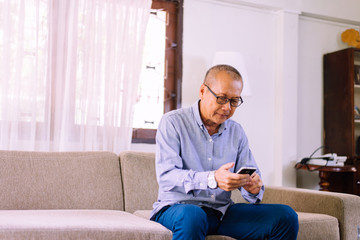 Senior asian man wearing glasses and using mobile phone at home,Relax time,Senior lifestyle concept,Long sighted