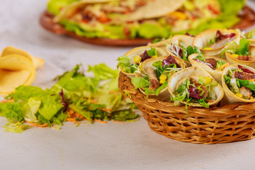 Tortillas cone stuffed with vegetable and meat on basket with green salad on white table.