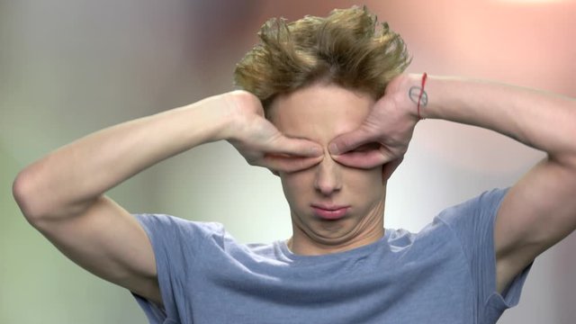 Funny teenage boy showing tongue. Adolescent male making silly grimace and teasing someone. Abstract blurred background.