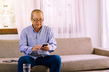Senior asian man wearing glasses and using mobile phone at home,Relax time,Senior lifestyle...