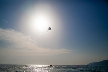 Fototapeta na wymiar Jet ski and skydiver in the sky over the sea. Summer outdoor activities on the water.