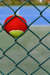 tennis ball stuck on the wire fence of a outdoor court vertical composition