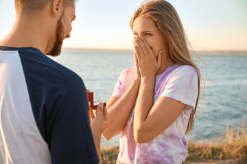 Young man proposing to his beloved near river