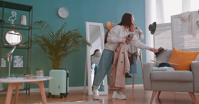 Caucasian young attractive girl blogger in flasses tryingon new coat and dancing with spinning in it in front of the mirror at home while doing video blog. Indoor.