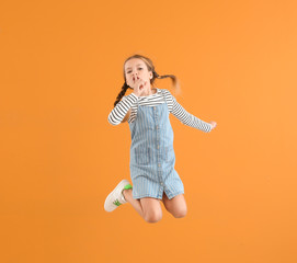 Jumping little girl showing silence gesture on color background