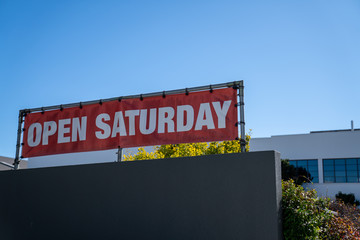 Open Saturday sign hanging on top of store building on sunny day