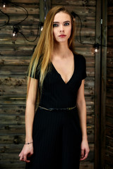 The concept of glamor, style. Vertical portrait of a pretty blonde girl with long hair and excellent make-up on a wooden background with lights. Standing in different poses in front of the camera.