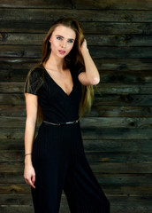 The concept of glamor, style. Model Stands in different poses in front of the camera. Vertical portrait of a pretty blonde girl with long hair and great makeup on a wooden background.