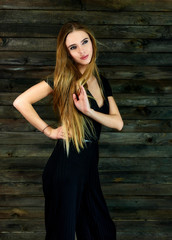 Fototapeta premium The concept of glamor, style. Model Stands in different poses in front of the camera. Vertical portrait of a pretty blonde girl with long hair and great makeup on a wooden background.