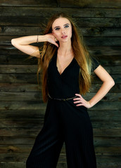Obraz premium The concept of glamor, style. Model Stands in different poses in front of the camera. Vertical portrait of a pretty blonde girl with long hair and great makeup on a wooden background.