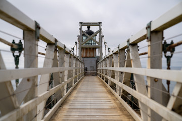 Fototapeta na wymiar Small white suspension bridge foot path leading to lighthouse