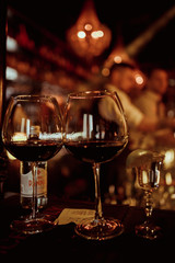 Low angle close up perspective of crystal clear wine glass with traditional round goblet shape filled with dark red wine and slim stem on wood counter top bar with blurry restaurant background scene