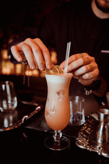 Bartender holding tongs in his hands adorns pink cocktail with an grapefruit slice. Barman at work, preparing cocktails