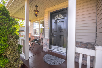 Home with chairs on porch and brown door with glass panes and welcome sign