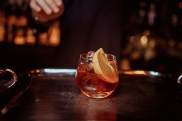 Bartender holding tongs in his hands adorns pink cocktail with an grapefruit slice. Barman at work, preparing cocktails
