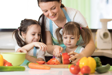 family mum with kids daughters chopping vegetables in home kitchen