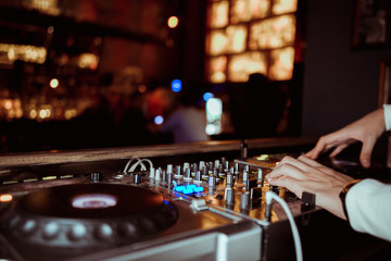 DJ plays live set and mixing music on turntable console at stage in the night club. Disc Jokey Hands on a sound mixer station at club party. DJ mixer controller panel for playing music and partying.