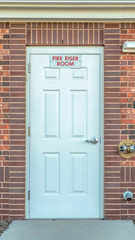 Vertical frame Fire Riser Room sign on the white wood door of a building with red brick wall
